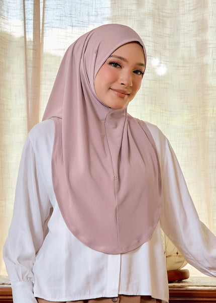 Woman wearing a pink hijab and white shirt in front of a beige curtain