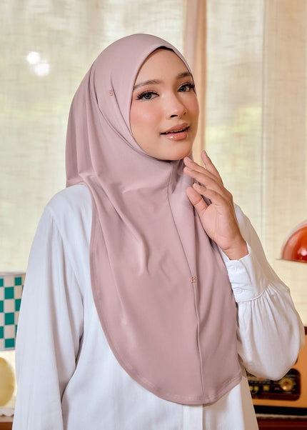 Woman wearing a pink hijab and white blouse in a room with a lamp and decorative items.