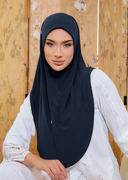 Woman wearing a black hijab and white lace top in front of a floral wooden panel.