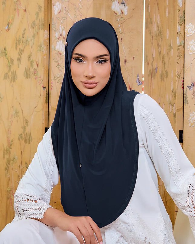 Woman wearing a black hijab and white lace top in front of a floral wooden panel.
