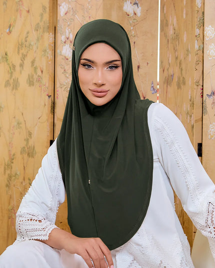 Woman wearing a green hijab and white lace dress against a wooden panel background