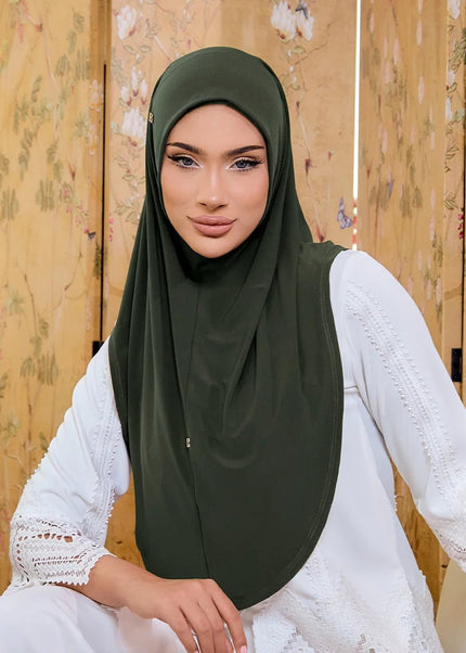 Woman wearing a green hijab and white lace dress against a wooden panel background