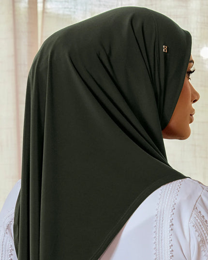 Woman wearing a black hijab with a white lace garment underneath, against a neutral background.